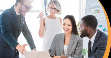 A diverse group of business professionals discussing ideas around a laptop, smiling and collaborating in a modern office setting.