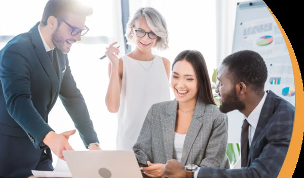 A diverse group of business professionals discussing ideas around a laptop, smiling and collaborating in a modern office setting.